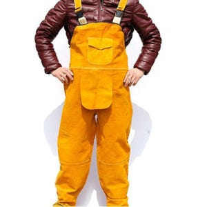 May include: Yellow leather work overalls with adjustable straps and a chest pocket. The overalls have reinforced knees and a large front pocket. The model is wearing a brown jacket.