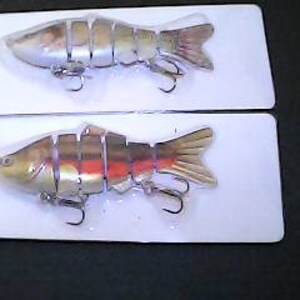 May include: Two plastic fishing lures, one with a silver and green body and the other with a gold and orange body. Both lures have a segmented body and realistic details.