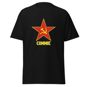 Może przedstawiać: Czarna koszulka z czerwoną gwiazdą i żółtym symbolem młota i sierpa. Słowo "COMMIE" jest wydrukowane na żółto pod gwiazdą. Koszulka ma krótki rękaw i okrągły dekolt.
