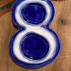 May include: A blue and white ceramic number eight. The number is outlined in white and has a glossy finish.