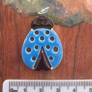 May include: A ceramic ladybug figurine with a bright blue body and black spots. The head and the V-shaped marking are also black. The ladybug is approximately 5 cm long.