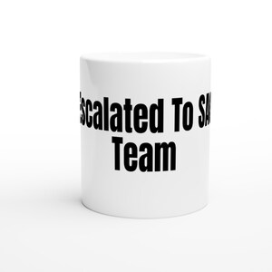 Może przedstawiać: Biały ceramiczny kubek z czarnym, pogrubionym napisem "Escalated To SA Team". Kubek jest cylindryczny i stoi na białej powierzchni. Projekt jest prosty i nowoczesny.