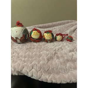 Puede incluir: Un conjunto de cinco adornos navideños con diseños de Papá Noel. Los adornos están pintados en rojo, blanco y verde. Cada adorno presenta una cara y un atuendo diferentes de Papá Noel, perfectos para la decoración festiva.