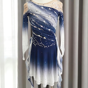 May include: A long-sleeved dress featuring a blue and white ombre gradient, a sheer nude-colored neckline, and diagonal ruching across the bodice. The garment is embellished with numerous clear and dark crystals arranged in a scattered pattern.