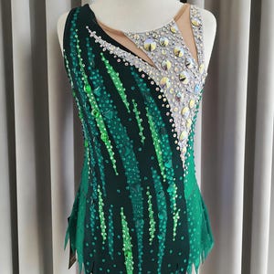 Può includere: Un body senza maniche con base verde scuro e strisce verticali di paillettes verde brillante e smeraldo. La parte superiore del petto presenta un inserto in rete beige decorato con grandi cristalli circolari dai riflessi iridescenti.