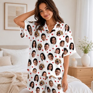 May include: A white short-sleeved button-down pajama shirt and matching shorts set featuring an all-over repeating pattern of various human faces and golden retriever dog faces interspersed with small red heart icons throughout the fabric.
