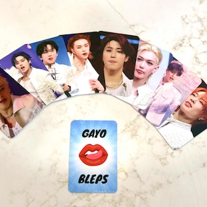 May include: A collection of fan-made photo cards featuring various individuals, arranged in a semi-circle. A blue card with the words "GAYO BLEPS" and a graphic of red lips is in the foreground.