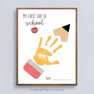 May include: A white poster with a wooden frame featuring the text MY FIRST DAY OF school and 2026 inside a red apple graphic. A yellow handprint is centered, positioned between a pink eraser graphic and a tan pencil tip. The word NAME is at the bottom.