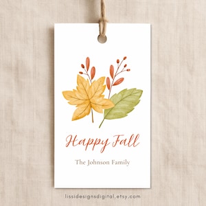 May include: A rectangular white gift tag with a hole at the top and a brown string. The tag features a watercolor illustration of yellow and green autumn leaves with orange berries. The text reads Happy Fall and The Johnson Family.