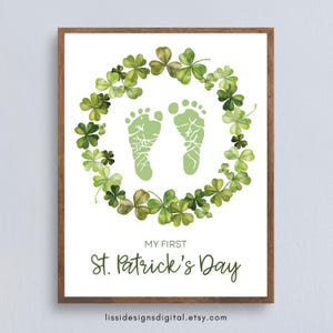 May include: A framed print featuring a green shamrock wreath surrounding two light green baby footprints. The text "MY FIRST St. Patrick's Day" is below the footprints. The print has a white background and a brown wooden frame.