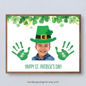 May include: A framed print for St. Patrick's Day featuring a child wearing a green leprechaun hat. Green handprints flank the child's smiling face. The words "HAPPY ST. PATRICK'S DAY!" are printed below the child. Green shamrocks and gold horseshoes decorate the top.