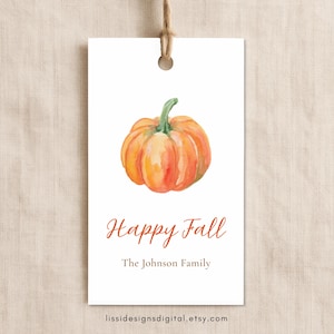 May include: A rectangular white gift tag with a watercolor orange pumpkin illustration at the top. The text reads Happy Fall in orange script and The Johnson Family in brown serif font. A brown string is attached through a hole at the top.
