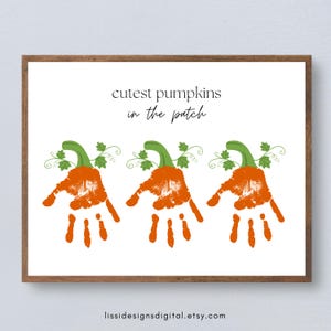 以下が含まれることがあります： 木製のフレームに入った長方形のプリントで、「cutest pumpkins in the patch」という文字と、3つのオレンジ色の手形イラストが描かれています。各手形の上部には緑色の茎と葉が添えられており、カボチャのような見た目になっています。