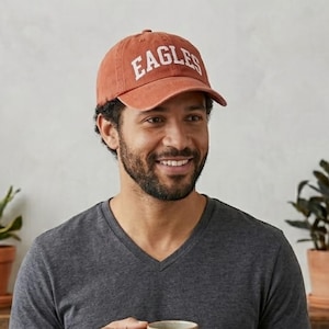 May include: A rust-colored baseball cap with the word "EAGLES" in white block letters. The cap is worn by a person wearing a gray v-neck shirt.