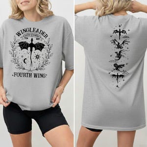 A woman wearing a grey t-shirt with a graphic design featuring a dragon and the text "WINGLEADER" and "FOURTH WING".