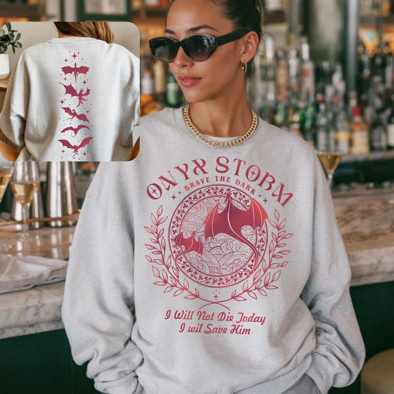 A woman wearing a grey sweatshirt with a graphic design featuring bats and a dragon, standing in front of a bar.