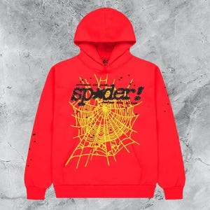 Op de afbeelding: Een rode hoodie met een geel spinnenwebontwerp en het woord "spider!" in zwart en geel. De hoodie met lange mouwen heeft kleine zwarte sterren.