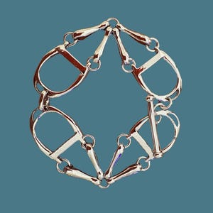 May include: A silver-toned metal bracelet featuring a repeating pattern of four stirrup-shaped links connected by smaller bar-shaped links. The bracelet is secured with a toggle clasp consisting of a straight bar and a circular ring.