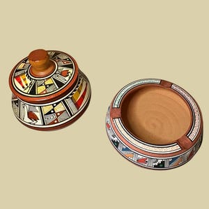 May include: A decorative ceramic jar with a lid and a matching ashtray. The jar and ashtray are painted with geometric patterns in red, yellow, black, and white. The jar has a wooden knob on top.