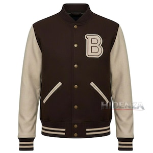 Könnte beinhalten: Braune Collegejacke mit beigen Ärmeln und einem Buchstaben "B"-Aufnäher. Die Jacke hat einen gerippten Kragen, Bündchen und Saum mit beigen und braunen Streifen. Mit Knopfleiste und zwei Vordertaschen mit weißer Paspelierung.