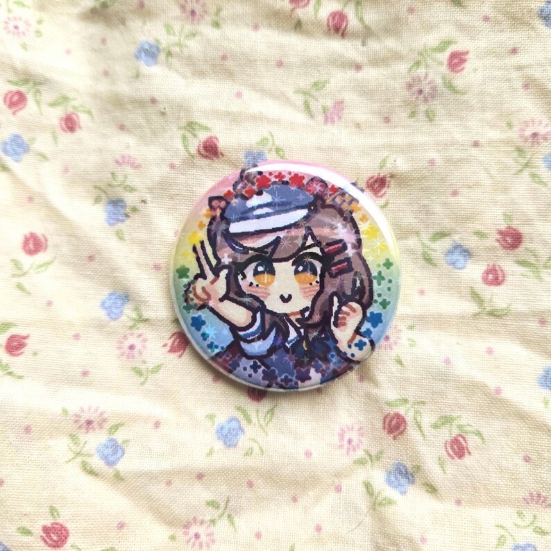 K&ouml;nnte beinhalten: Ein runder Ansteckbutton mit einer Anime-Illustration eines M&auml;dchens in Matrosenkleidung. Der Button hat einen Regenbogenrand und liegt auf einem Stoff mit Blumenmuster.