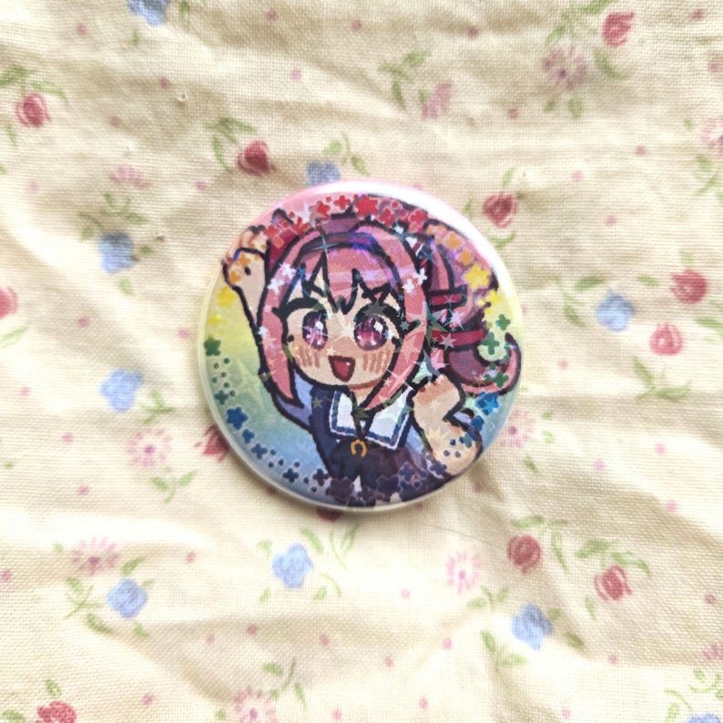 K&ouml;nnte beinhalten: Ein runder Ansteckbutton mit holografischer Oberfl&auml;che und einer bunten Anime-Illustration einer Figur mit rosa Haaren, einem dunkelblauen Outfit mit Kragen und einem fr&ouml;hlichen Gesichtsausdruck vor einem leuchtenden Regenbogenhintergrund.