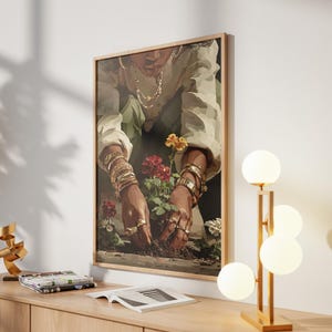 May include: A framed art print depicts a person tending to flowers, adorned with gold jewelry. The artwork is set against a neutral wall, complemented by a modern lamp with spherical lights and a wooden cabinet. A gold sculpture and magazines are also on the cabinet.