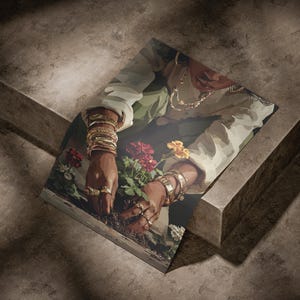 May include: An art print featuring a person tending to flowers. The person is wearing gold jewelry, including bracelets and rings. The artwork has a warm color palette with red and yellow flowers.
