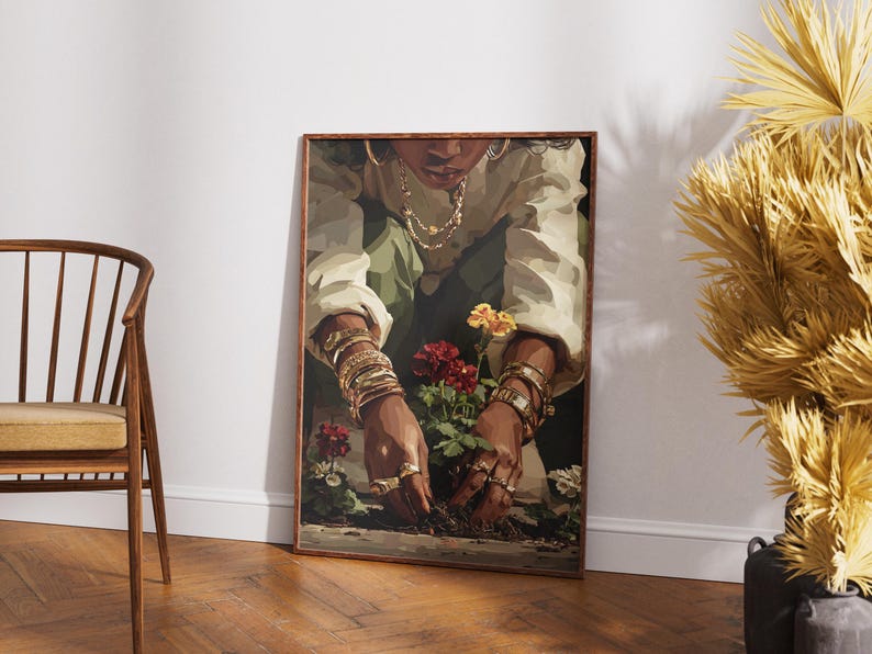 May include: A framed art print depicts a person tending to flowers. The person is wearing gold jewelry and a white shirt. The flowers are red, yellow, and white. The artwork is displayed on a white wall next to a wooden chair and dried plants.