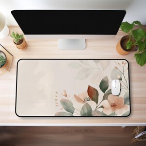 May include: Rectangular mouse pad with a black border. The pad features a watercolor floral design with peach and brown flowers, green leaves, and a light beige background. A white computer mouse rests on the pad.