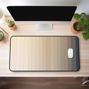 May include: A rectangular mouse mat with a black border features a gradient design of vertical stripes in shades of beige, tan, and grey. A white computer mouse is positioned on the right side of the mat. The mat is on a light wood desk.