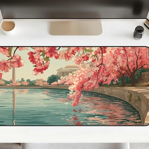 May include: A rectangular desk mat featuring a scenic illustration of cherry blossoms in Washington, D.C. The image includes the Washington Monument, the Jefferson Memorial, and a body of water. The color palette includes pink, green, and blue.