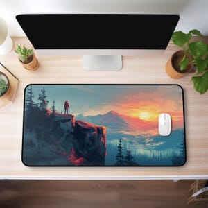 May include: A rectangular mouse pad featuring a landscape painting of a person standing on a cliff, overlooking a mountain range at sunset. The color palette includes shades of orange, blue, and green. A white computer mouse is on the right side of the pad.
