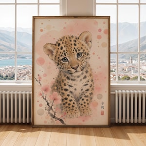 May include: A framed watercolor print of a baby leopard with a soft, spotted coat and blue eyes. The artwork features a pink and beige background with cherry blossoms and Japanese text. The print is displayed in a room with a window.