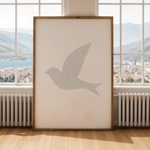 May include: A framed print depicting a dove silhouette made of small black dots. The artwork is set against a cream background and framed in natural wood. The print is displayed in a room with a window overlooking a cityscape.