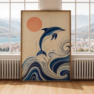 May include: Framed art print depicting a dolphin leaping from ocean waves. The artwork uses shades of blue and white against a beige background, with a peach-coloured sun in the upper left corner. The print is in a wooden frame.