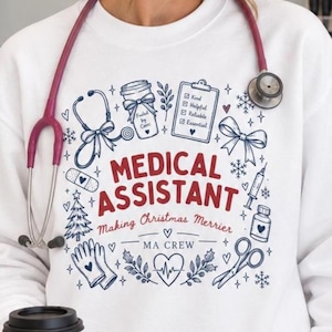 May include: A white long-sleeve sweatshirt featuring a graphic print with the text MEDICAL ASSISTANT Making Christmas Merrier MA CREW, surrounded by illustrations of a stethoscope, clipboard, syringe, gloves, scissors, and holiday motifs.
