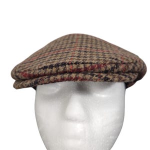 May include: A brown and tan plaid flat cap with red and navy accents. The hat is made of a textured fabric and has a rounded crown and a small, stiff brim. This classic style is suitable for various occasions.
