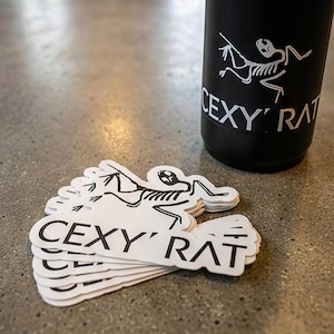 Könnte beinhalten: Schwarzer Becher und Aufkleber mit einem Skelett-Motiv. Die Aufkleber und der Becher zeigen den Text "CEXY' RAT" in fetter Schrift. Das Skelett-Motiv ist weiß und der Becher ist schwarz.
