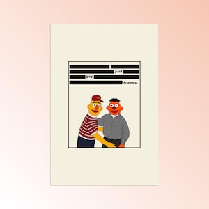 Op de afbeelding: Een rechthoekige print met twee gele en oranje popfiguren die naast elkaar staan. Het linkerfiguur draagt een rode pet en een gestreept shirt, het rechterfiguur een grijs overhemd. Zwarte balken verbergen tekst erboven, waardoor alleen de woorden "just", "gay" en "friends." zichtbaar blijven.