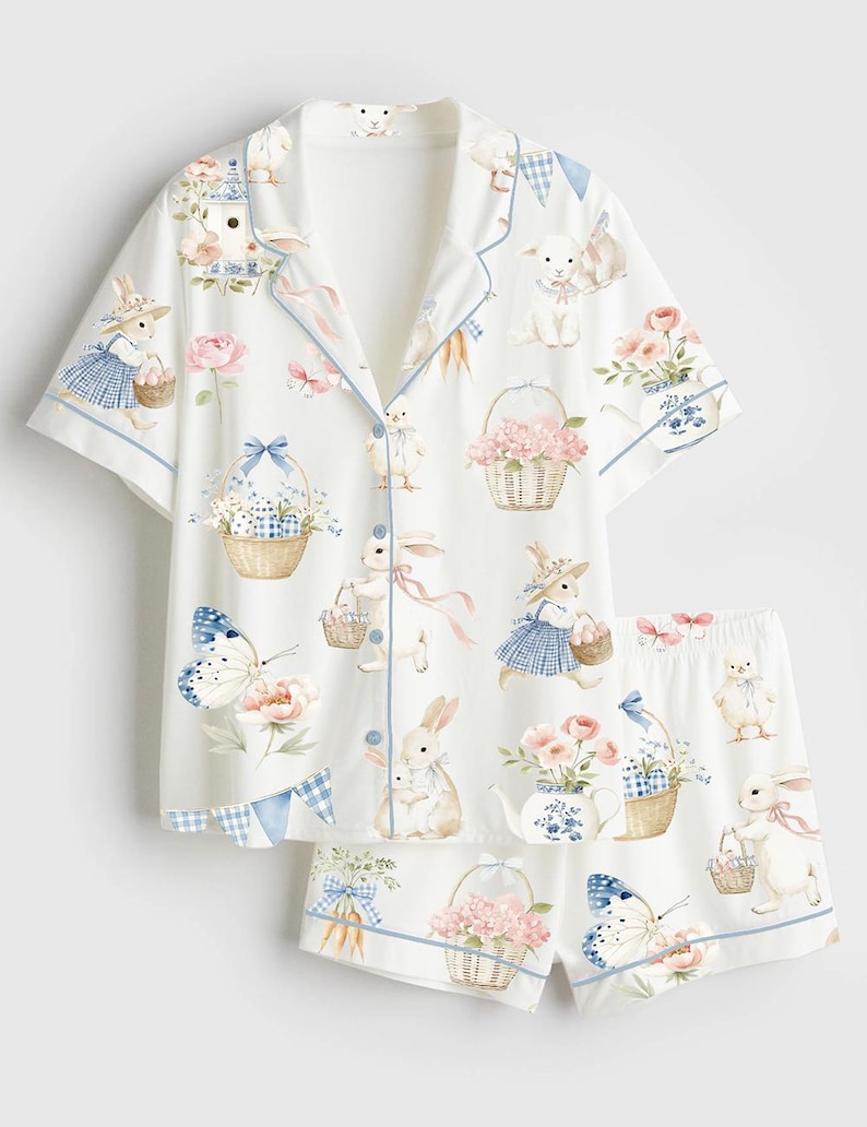 Op de afbeelding: Witte pyjamaset met een konijnen- en bloemenprint. De top met korte mouwen en de shorts hebben een herhalend patroon van konijnen, manden, vlinders en bloemen in pastelkleuren, afgezet met blauwe biezen.