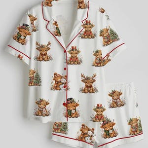 May include: A white short-sleeve button-down pajama shirt and matching shorts set featuring a repeating print of Highland cattle in various holiday-themed outfits, including scarves, hats, and Christmas trees, finished with red piping trim.
