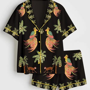 May include: Black pajama set with a tropical print. The short-sleeved shirt and shorts feature colorful parrots, monkeys, palm trees, and pineapple designs. The set is trimmed with yellow piping.