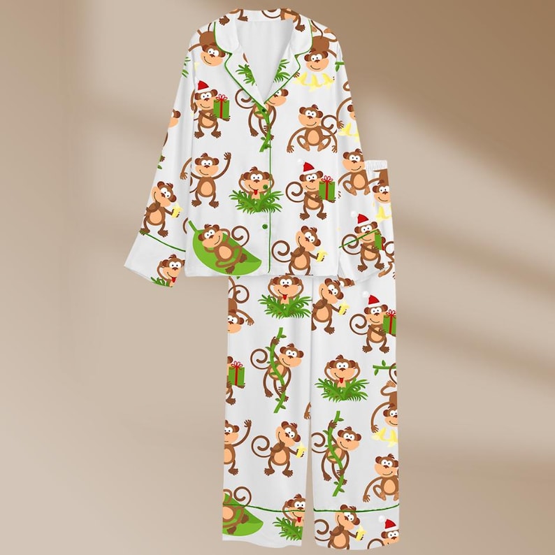 May include: White pajama set with a repeating pattern of cartoon monkeys in various poses. The monkeys are brown with red Santa hats and green gift boxes. The pajamas have green trim.