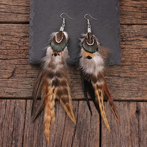 May include: A pair of drop earrings featuring layered natural feathers in shades of brown, tan, and white, topped with a small iridescent teal and black patterned feather accent and silver-toned metal hooks for secure attachment to the ear.