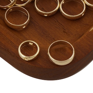 May include: A close-up of a group of gold-colored metal rings with small holes on a wooden surface. The rings are arranged in a random pattern.