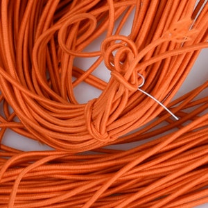 May include: A close-up of a large bundle of orange elastic cord. The cord is tightly wound and appears to be made of a soft, stretchy material.