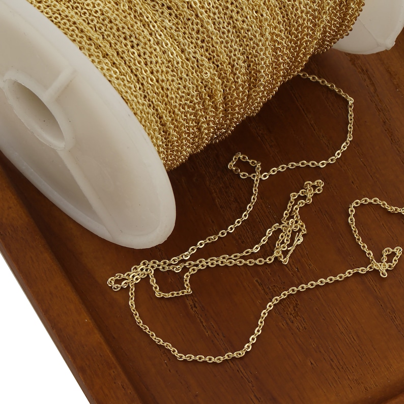 May include: A spool of gold chain, with a length of chain laid out on a wooden surface. The chain is a fine, delicate style.