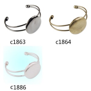 May include: Three silver and gold tone bangle bracelets with a round locket charm. The lockets are blank and can be personalized.