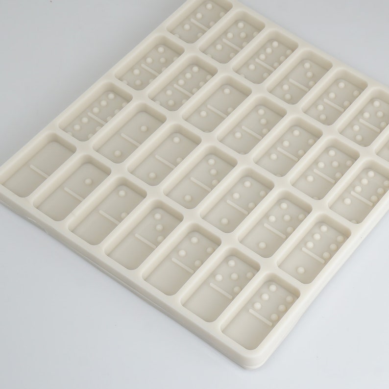 May include: A white silicone mold with 28 rectangular cavities shaped like dominoes. The mold is designed for making chocolate or candy dominoes.
